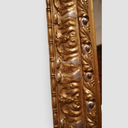 Ornate antique trapezoidal wall mirror with decorative gilt frame and crest